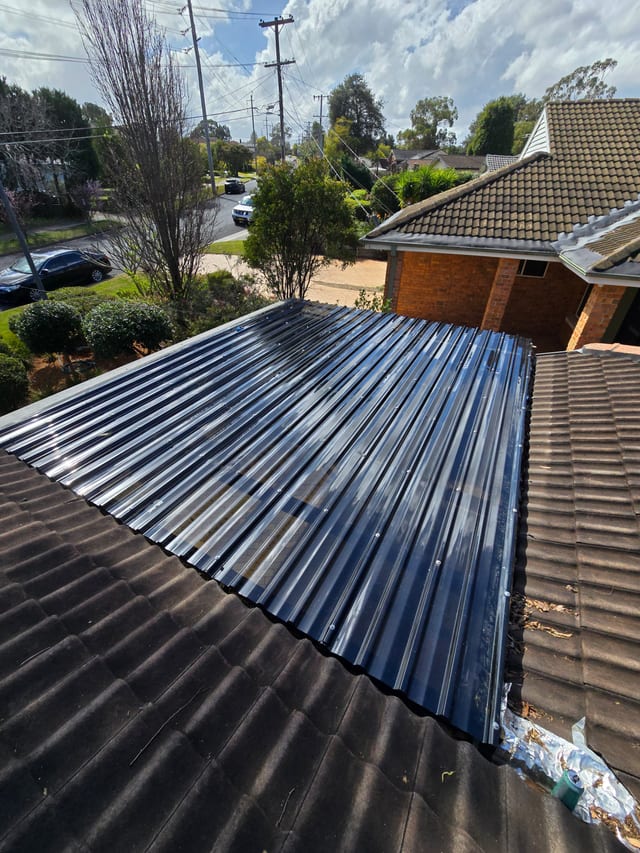 Sydney roofer kneeling on a tile roof inspecting ridgecaps with tools beside him